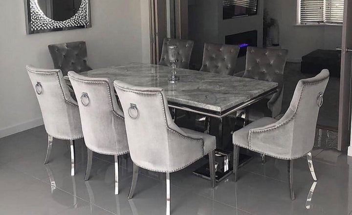 A marble dining table with a light grey finish accompanied by silver ring knocker chairs.