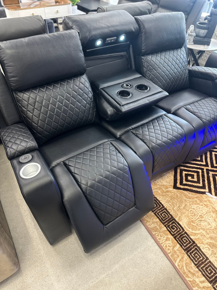 Black leather recliner seats with cup holders and armrests in a showroom setting.