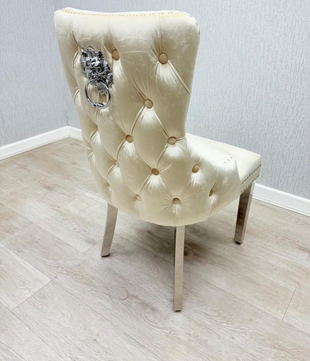 A cream-colored dining chair with a tufted backrest and a decorative lion and ring knocker on the back.