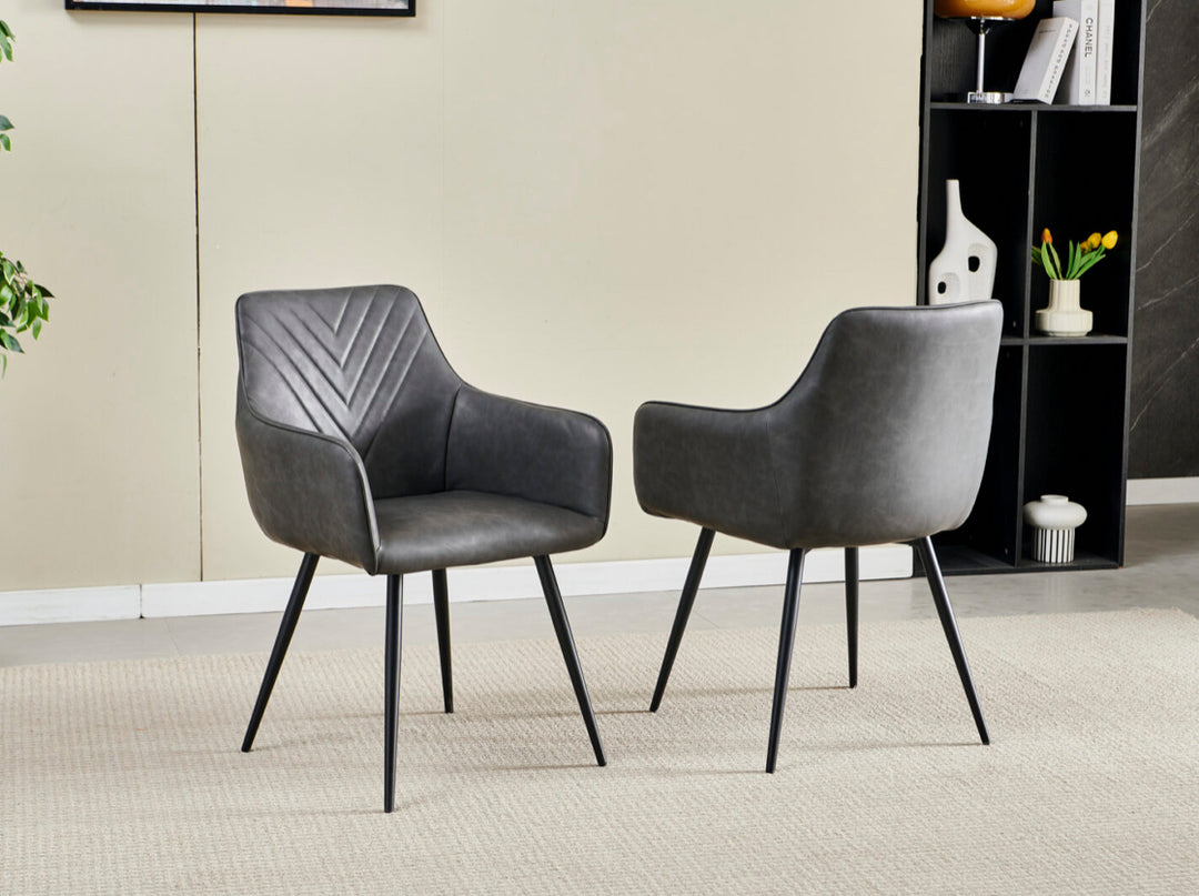 A pair of gray leather dining chairs with black metal legs in a room setting.