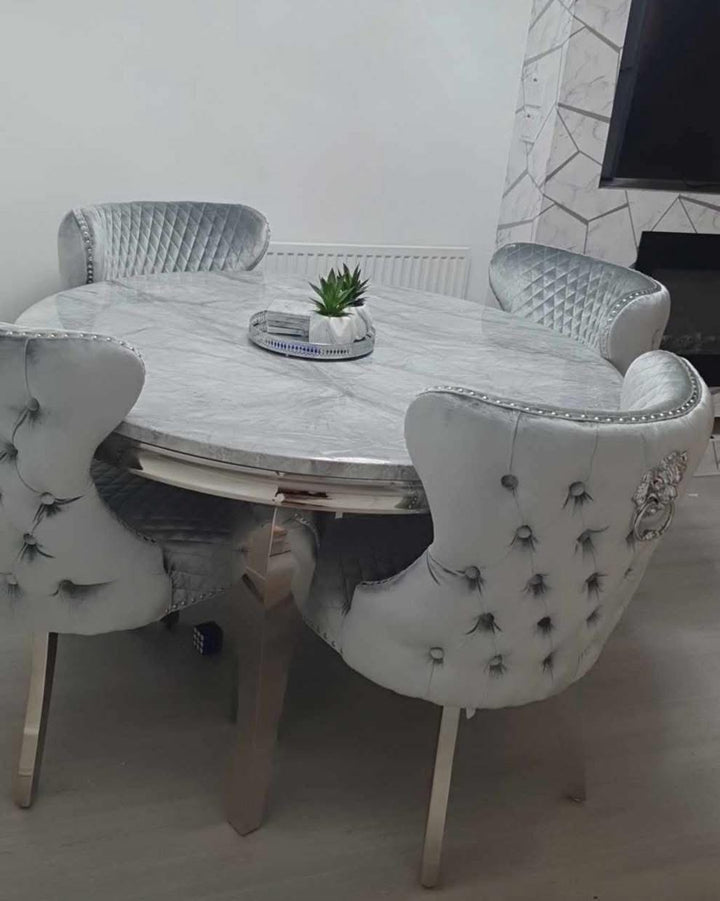 A round dining table with a grey marble-like finish accompanied by four upholstered dining chairs with a tufted design and silver accents on the legs.